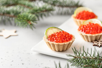 Festive Christmas appetizer tartlets stuffed with red caviar and a slice of lime on white background with fir branches. Christmas or new year holiday party concept, food recipe