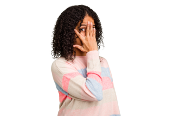 Young Brazilian curly hair cute woman isolated blink at the camera through fingers, embarrassed covering face.
