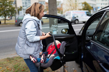 Obraz na płótnie Canvas a young woman puts a car seat for a one-year-old child in a car