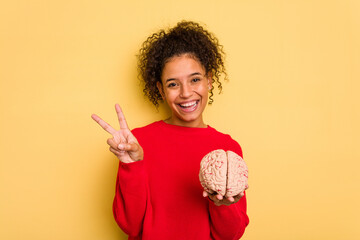 Young brazilian woman holding a brain model isolated joyful and carefree showing a peace symbol...