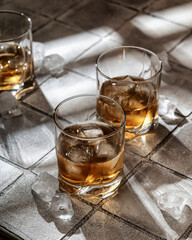 Whiskey with ice in glasses. Gray tile background. Hard light, copy space