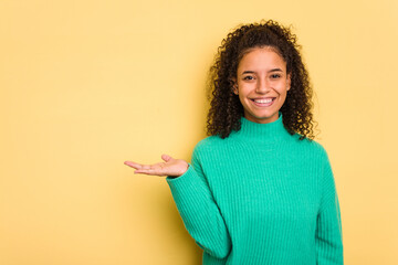 Young Brazilian curly hair cute woman isolated on yellow background showing a copy space on a palm...