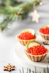 Festive Christmas appetizer tartlets stuffed with red caviar and a slice of lime on white background with fir branches. Christmas or new year holiday party concept, food recipe