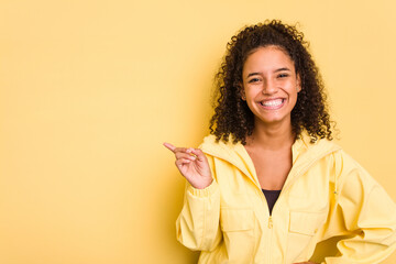 Young Brazilian curly hair cute woman isolated on yellow background smiling cheerfully pointing...