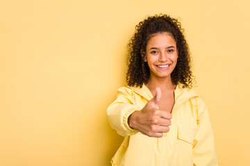 Young Brazilian curly hair cute woman isolated on yellow background smiling and raising thumb up