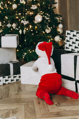 Obraz premium a small child looks at gifts under the tree in a Santa costume