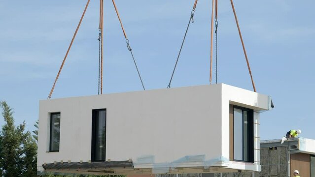 Modern modular home unit hanging by crane lift to set in foundation site