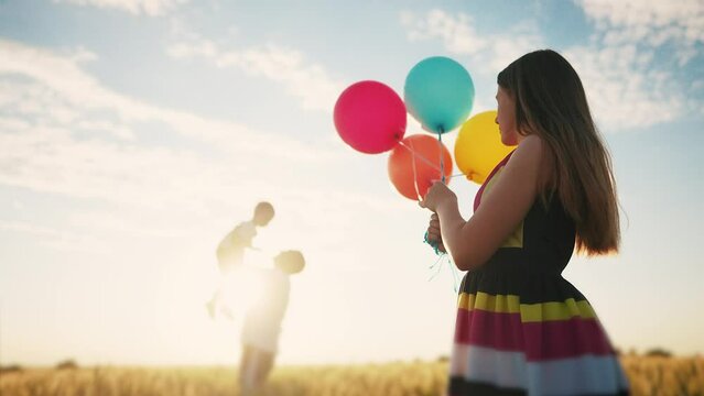 happy family celebrates birthday in the park. girl a holding colorful balloons silhouette in the field. dad throws his son into the sky in the park lifestyle. happy family kid dream concept