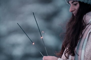 Happy new year,portrait of a happy  beautiful brunette girl in the snow, with winter hat and warm gloves in the sunny winter day,Outdoor waist up portrait,girl holding sparklers, New Year's Eve