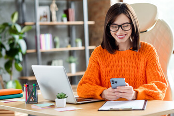 Photo of positive attractive lady wear orange sweater smiling connecting clients modern device indoors workshop workplace workstation