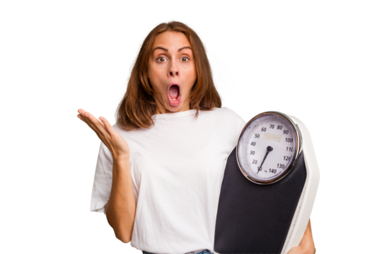 Young caucasian woman holding a scale and measure tape isolated surprised and shocked.