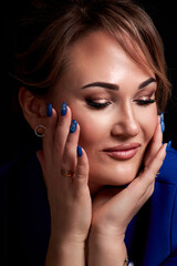Fototapeta na wymiar portrait of a beautiful caucasian woman in a blue jacket holds her hands near her face on a black background