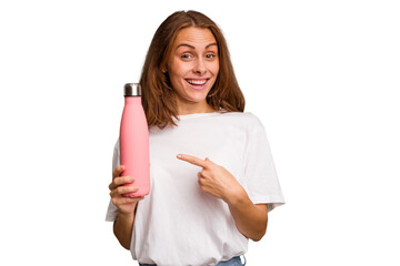 Young caucasian woman holding a pink thermo isolated smiling and pointing aside, showing something...