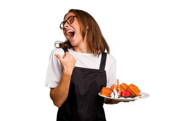 Young caucasian woman holding a waffles dish isolated points with thumb finger away, laughing and carefree.