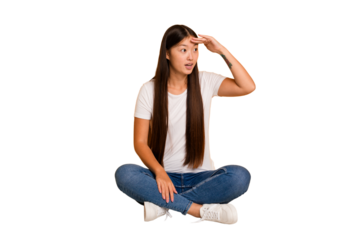 Young asian woman sitting on the floor cutout isolated looking far away keeping hand on forehead.