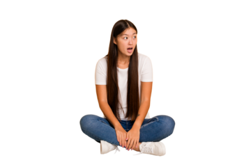 Young asian woman sitting on the floor cutout isolated being shocked because of something she has seen.