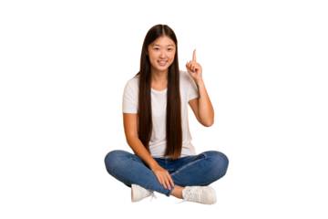Young asian woman sitting on the floor cutout isolated showing number one with finger.