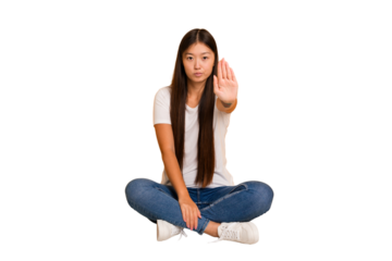 Young asian woman sitting on the floor cutout isolated standing with outstretched hand showing stop sign, preventing you.