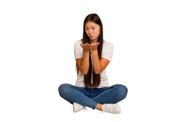 Young asian woman sitting on the floor cutout isolated folding lips and holding palms to send air kiss.