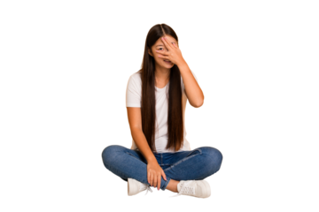 Young asian woman sitting on the floor cutout isolated blink at the camera through fingers, embarrassed covering face.