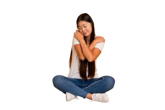 Young asian woman sitting on the floor cutout isolated hugs, smiling carefree and happy.