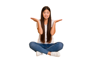 Young asian woman sitting on the floor cutout isolated confused and doubtful shrugging shoulders to hold a copy space.