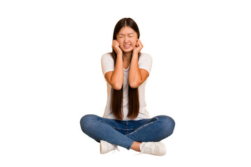 Young asian woman sitting on the floor cutout isolated covering ears with hands.