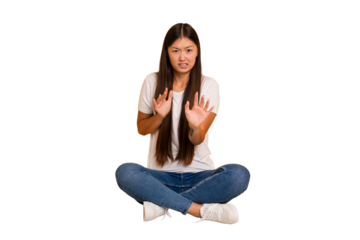 Young asian woman sitting on the floor cutout isolated rejecting someone showing a gesture of disgust.
