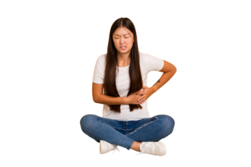 Young asian woman sitting on the floor cutout isolated having a liver pain, stomach ache.