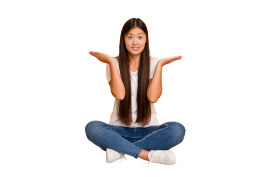 Young asian woman sitting on the floor cutout isolated confused and doubtful shrugging shoulders to hold a copy space.