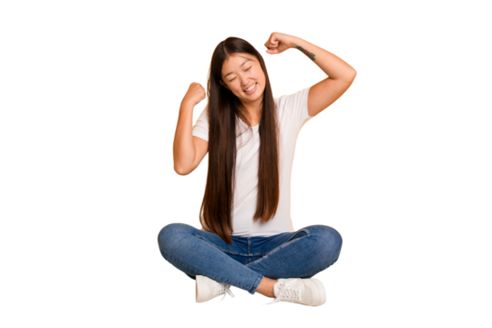Young asian woman sitting on the floor cutout isolated celebrating a special day, jumps and raise arms with energy.