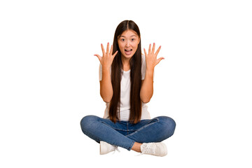 Young asian woman sitting on the floor cutout isolated receiving a pleasant surprise, excited and raising hands.