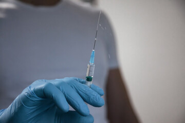 Close up man doctor hand in blue latex gloves holding syringe with medical vaccine injection, liquid drug or narcotic. Medicine vaccination syringe with needle, health care in clinic. Copy space