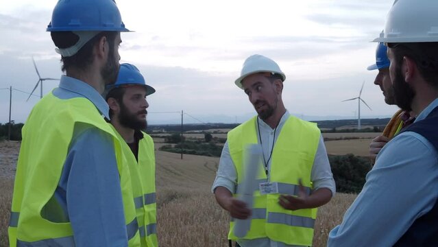 Group of workers and male engineers brainstorming in a field of windmills