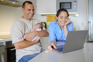 Obraz premium Sensual mother and father with sleeping baby watching photos on laptop