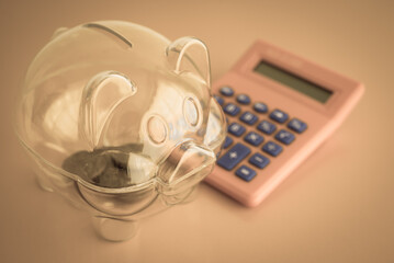 Very little money coins in clear piggy bank and calculator. No planning or knowledge for money...