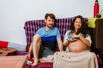 man sitting next to his pregnant wife in the living room resting, looking at the camera.