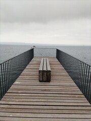 Obraz premium Ponton de lac en bois avec mouettes posées sur la rambarde sur fond de ciel gris.