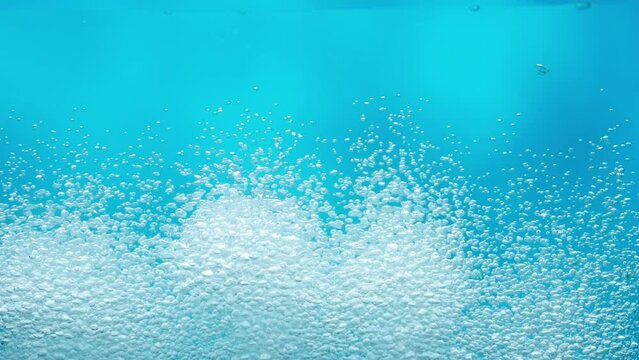 Shiny air bubbles underwater rising from bottom to surface and illuminated by rays of light. Stream of oxygen bubbles in blue ocean or sea water. Close up of bubbling liquid in aquarium. Slow motion.
