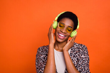 Portrait of attractive dreamy cheerful trendy carefree girl listening hit pop isolated over vivid orange color background