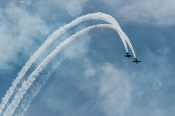 two small planes fly in parallel describing a white trajectory over the blue sky. condensation...