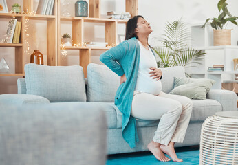 Obraz premium Pregnant, woman and back pain with a mother feeling painful body while sitting on her couch. Ache, inflammation and pregnancy with a maternity female with physical strain in her back at home