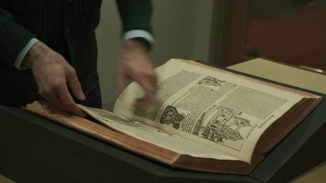 Librarian flipping through medieval book, Nuremberg chronicle, pointing at images and text