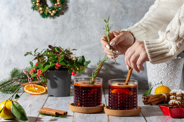Mulled wine in glasses on white wooden table in Christmas decoration. Female hands preparing hot...