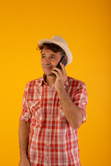 Dark-haired man in a hat and colored shirt on an orange background with a mobile phone in different poses, calling, listening, touching or celebrating something he has seen on the screen