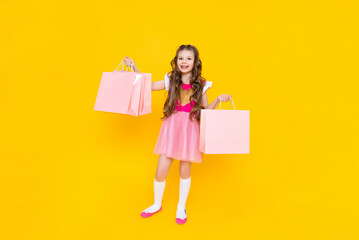 Fototapeta premium New purchases for the summer, a little girl returns from the store with large bags of things. A child in a pink dress with shopping bags on an isolated background.