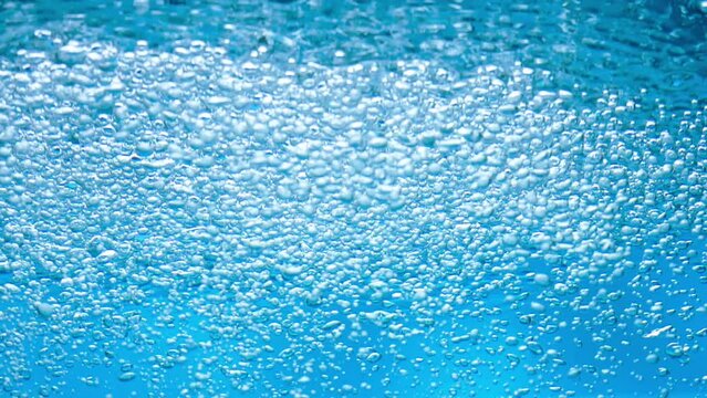 A stream of air bubbles rising onto the surface of blue water from the depth. Close up of oxygen bubbles appearing on the surface of the liquid and bursting. Water bubbling, aeration. Slow motion.
