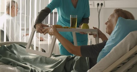 Nurse serving senior female patient meal in hospital bed