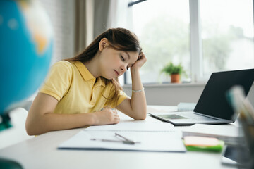 Fototapeta premium tired girl with closed eyes sitting near laptop with blank screen at home on blurred foreground