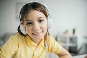 Naklejka premium portrait of happy preteen girl listening music in headphones and smiling at camera